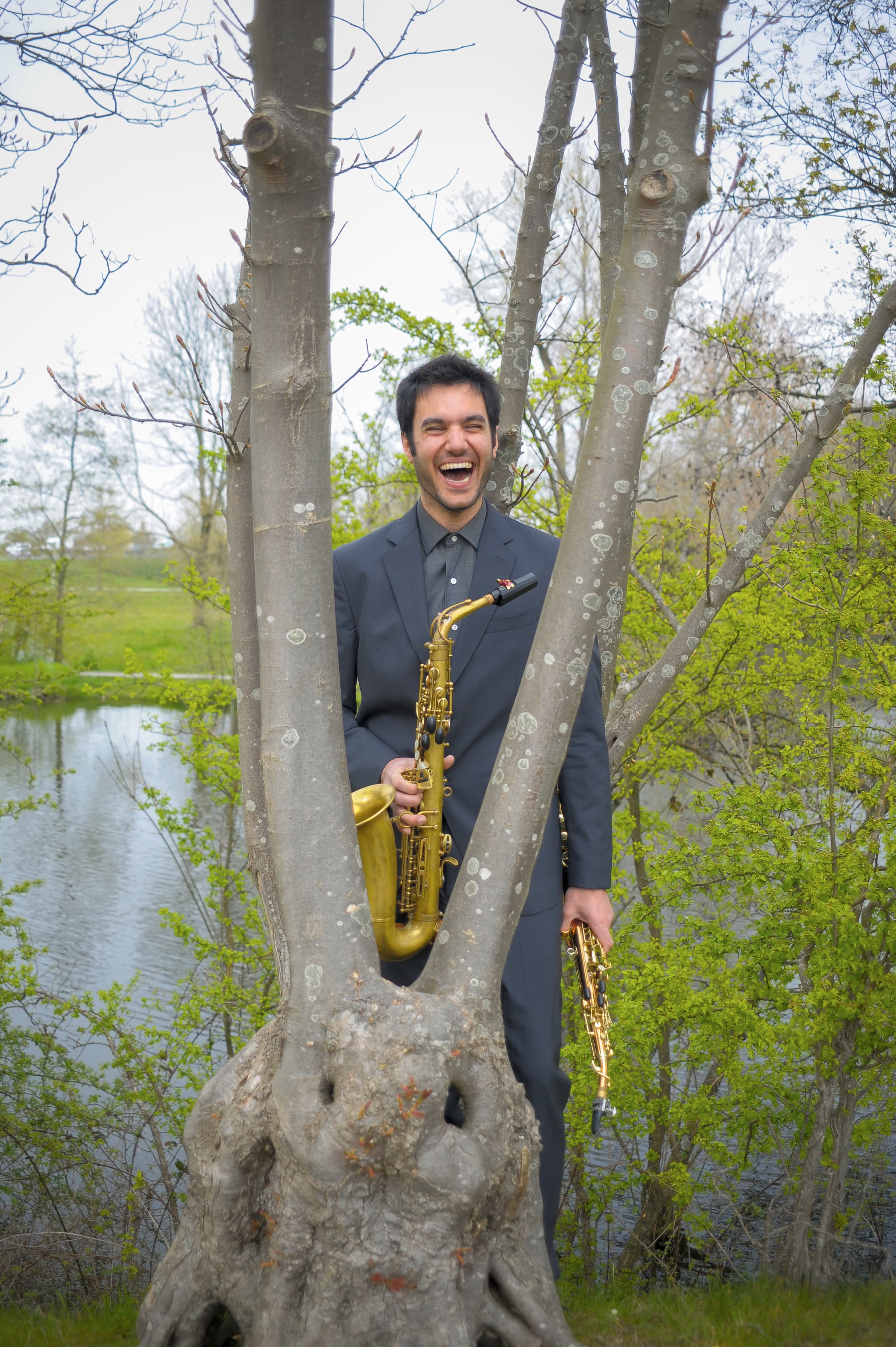 the artist holding his saxophone, smiling behind a tree